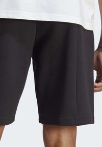 Mustat urheilu shortsit, jotka on valmistettu sileästä kankaasta. Niissä on suora leikkaus, joustava vyötärö ja ommellut helma-yksityiskohdat.