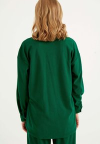 Grünes, geripptes Langarmshirt mit herunterfallenden Schultern, Manschetten mit Knöpfen und abgerundetem Saum, aus weichem Stoff gefertigt.