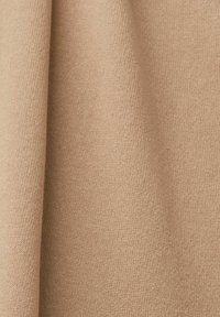 Tissu beige en maille avec une texture douce et des plis subtils sous une lumière naturelle.