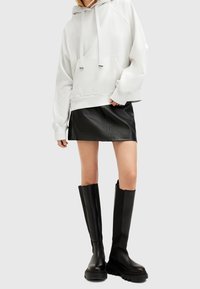 Witte oversized hoodie met trekkoorden, gecombineerd met een zwarte leren minirok en zwarte platformlaarzen tot aan de knie. Gladde texturen, casual ontwerp.