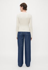 Ribbed, cream long-sleeve top paired with wide-leg, dark blue denim jeans featuring contrasting stitching and back pockets.