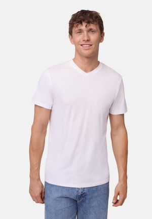 T-shirt bianca a collo a V realizzata in tessuto morbido, con maniche corte e taglio aderente, indossata con jeans in denim blu. Design semplice e pulito.