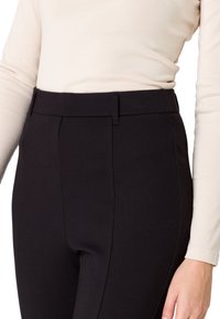 Pantalon noir taille haute avec une texture lisse, doté d'une ceinture et de jambes fuselées, associé à un haut léger à manches longues.