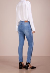 Ljust blåa tajta jeans med hög midja, kontrasterande sidostråk och bakficka. Bärs med en lång vit skjorta och svarta skor.