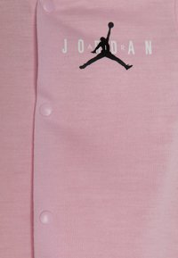 Cárdigan de color rosa con un logo negro "Jumpman" y el texto "JORDAN" en blanco. Tiene botones a presión rosas a juego en la parte frontal.