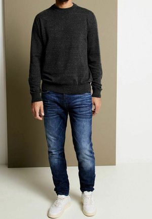 Dunkelgrauer Strickpullover mit rundem Ausschnitt, kombiniert mit blauen Jeans und weißen Turnschuhen. Die Textur wirkt weich und lässig.