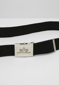 Svart nylongärd med en silverfärgad metallspänne som har "Alpha Industries USA"-logotypen. Hållbar, vävd textur med rektangulär form.