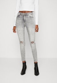 Šedé úzké džíny s opranými detaily, s roztrženími na kolenou. Kombinovány s černými kotníkovými botami a bílým crop topem.