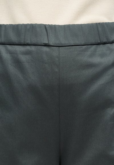 Σκούρο γκρι παντελόνι με ελαστική μέση, φορεμένο με ανοιχτό μπεζ πλεκτό τοπ, που δείχνει την υφή του υφάσματος και τη λεπτομέρεια της κεντρικής ραφής.