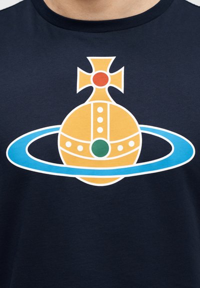 Μπλε ναυτικό T-shirt με γραφικό σχέδιο ενός κίτρινου σφαιρικού σχήματος με μπλε δαχτυλίδι, κόκκινες και πράσινες πινελιές και διακοσμητικό στοιχείο σε σχήμα σταυρού στην κορυφή.