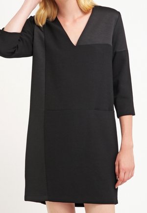 Robe noire avec un décolleté en V, des manches trois-quarts et un design en panneaux présentant une texture lisse et mate. Minimaliste et longueur genou.