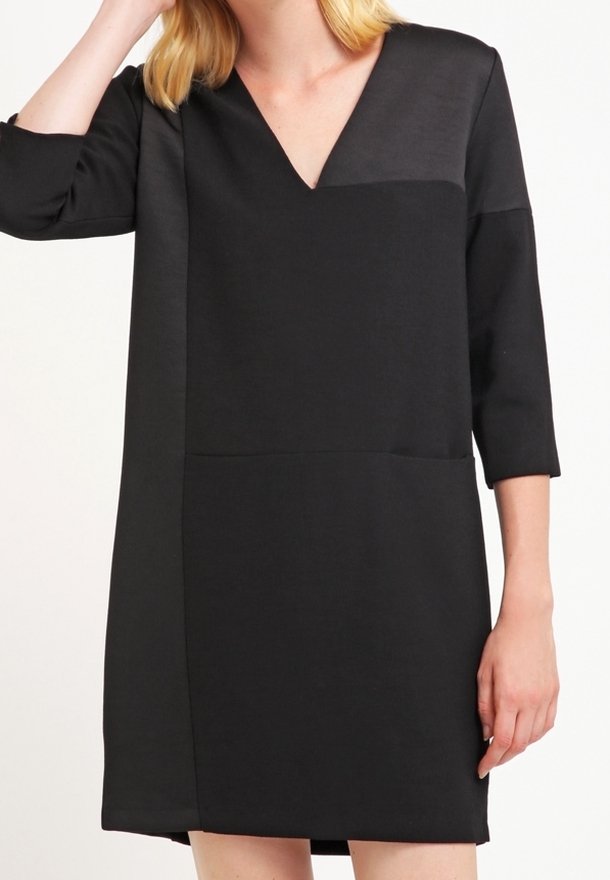 Robe noire avec un décolleté en V, des manches trois-quarts et un design en panneaux présentant une texture lisse et mate. Minimaliste et longueur genou.