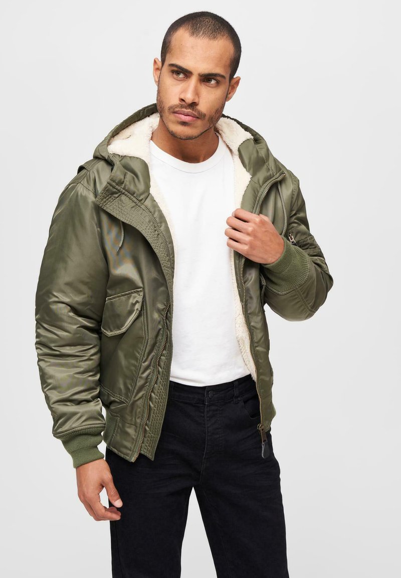 Olivgrön bomberjacka med dragkedja framtill, faux shearling-foder och ribbade muddar. Har två framfickor och avtagbar huva.