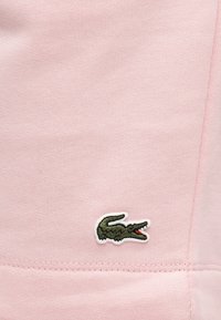 Μικρό πράσινο λογότυπο κροκοδείλου κεντημένο σε ελαφρύ ροζ πλεκτό ύφασμα κοντά σε ραφή.