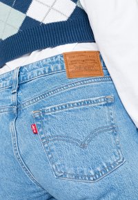 Jean en denim bleu clair avec un patch en cuir Levi's au dos, présentant un design de poche classique et un détail de languette rouge.