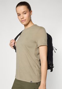 Camisa de manga corta verde oliva, hecha de tela suave, combinada con una mochila negra con tirantes ajustables y acentos texturizados.
