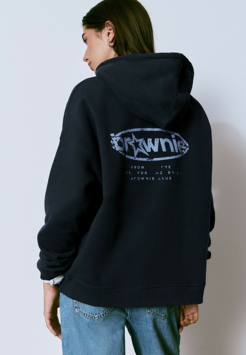 Sudadera negra con un gran gráfico en la parte posterior que presenta la palabra "brownie" y un diseño de estrellas. Tela suave, corte holgado y bolsillo tipo canguro.