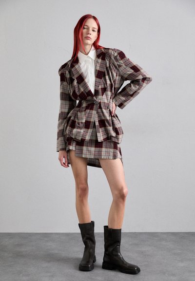Blazer de cuadros en tonos apagados con mangas abullonadas, combinado con una falda mini a juego. La modelo lleva botas negras hasta la rodilla. Tejido texturizado.