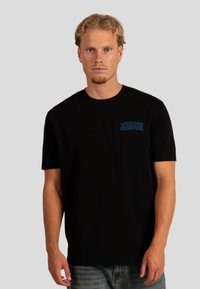 Czarna koszulka z krótkim rękawem z bawełny, z niebieskim napisem "WRONG FRIENDS" na lewej części klatki piersiowej. Standardowy krój i gładka tekstura.