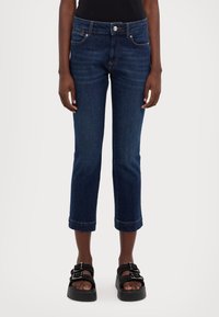 Tmavě modré džíny s krátkým střihem, těsně přiléhající v pase, přední kapsy a manžetový lem. V kombinaci s černými sandály na platformě s dvojitými přezkami.