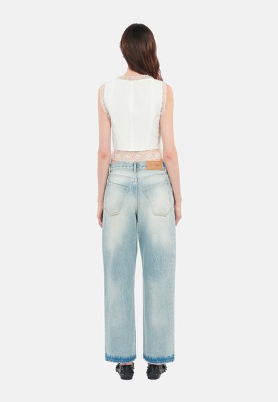 White cropped top with lace trim and light blue wide-leg jeans, featuring a faded appearance and two back pockets. Black heeled shoes visible.