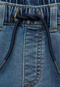 Jeansshorts med dragsko i midjan i mörk marinblått snöre. Ljt blått tyg med framträdande sömmar i gyllene tråd och lätt textur.