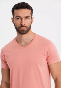 Růžové tričko s výstřihem do V, vyrobené z měkké látky, s přiléhavým střihem, krátkými rukávy, hladkým povrchem a jemným prošitím.
