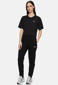 Zwarte crop top met korte mouwen met een witte FILA-logo, gecombineerd met zwarte joggerbroeken met een geborduurd FILA-logo en een elastische tailleband.