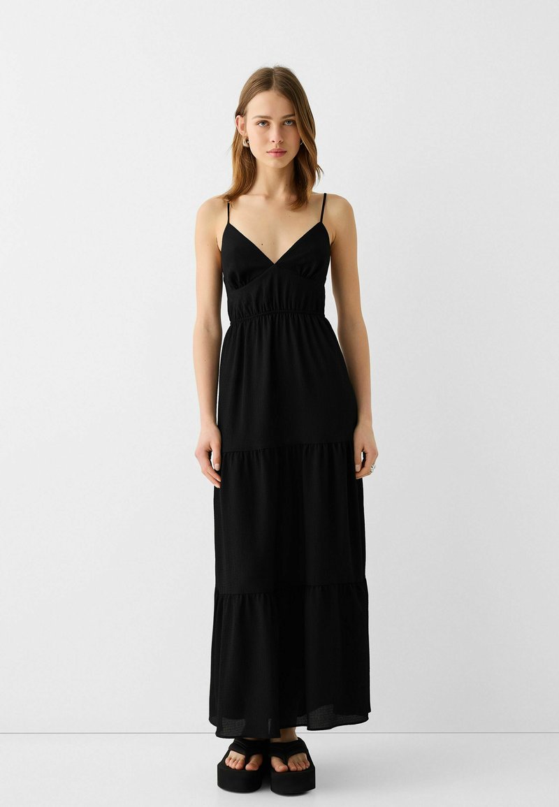 Robe maxi noire à volants avec des bretelles fines, un corsage ajusté et un tissu texturé. Associée à des sandales à plateforme épaisses.