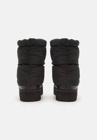 Pair of black insulated winter boots with thick cushioned shafts and flat soles, shown from the back on a white background.