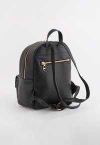 Sac à dos en cuir noir avec une forme structurée, fermetures éclair dorées, poche avant, bretelles ajustables et finition texturée.