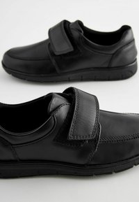 Chaussures en cuir noir avec une sangle Velcro, bout arrondi et accents texturés. Dotées de semelles en caoutchouc robustes pour une bonne adhérence et une durabilité.