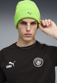 Puma neon grøn strikket hue med ribbet tekstur, parret med en sort jersey med hvide logoer og detaljer på skuldrene.