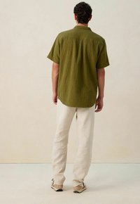 Olijfgroene shirt met korte mouwen van een gestructureerde stof, relaxte pasvorm en rechte zoom. Gecombineerd met lichtbeige linnen broek en beige schoenen.