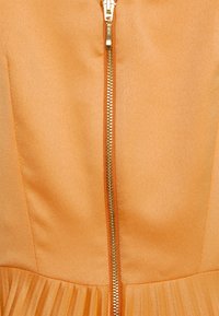 Robe orange sans manches avec fermeture zippée dorée, tissu texturé et détail de jupe plissée. Fini brillant et corsage ajusté.