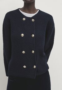 Granatowy sweter z dzianiny o teksturowym wykończeniu, z sześcioma guzikami w odcieniu złota ułożonymi w dwóch rzędach oraz okrągłym dekoltem.