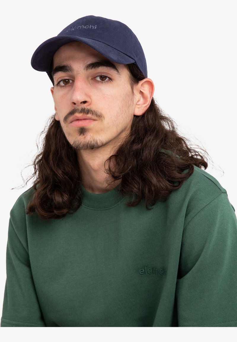Casquette marine avec une visière incurvée, ornée d'une broderie tonale "element" ; associée à un sweatshirt vert à col ras du cou, ayant une texture lisse.