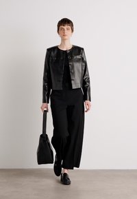 Black leather cropped jacket with round buttons, paired with black wide-leg trousers and a structured black bag. Model stands against a plain background.