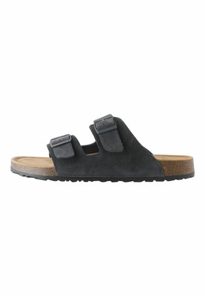 Schwarze Slides-Sandale mit zwei verstellbaren Schnallenriemen, Kork-Fußbett und strukturierter Gummisohle, von der Seite auf weißem Hintergrund gezeigt.
