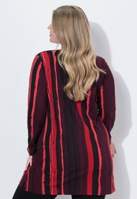 Long tunic in a patterned fabric featuring vertical stripes of deep red, black, and lighter red. Soft texture with long sleeves.