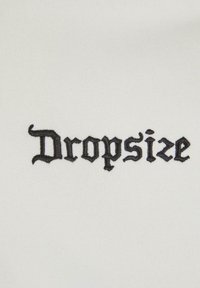 Tissu blanc avec le mot "Dropsize" brodé en lettres gothiques noires. La texture est lisse et légèrement extensible.