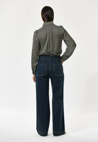 Svart och vit mönstrad blus med puffärmar, kombinerad med högmidjade mörkblå vida jeans med bakfickor och kontrasterande sömnad.