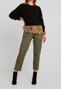 Svart sweatshirt med raglanärmar lager på en flerfärgad rutig skjorta. Olivgrön cargobyxa och svarta ankelstövlar fulländar outfiten.