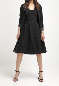 Zwarte oogjes kant rok met een uitlopende silhouet, gedetailleerde zoom, gecombineerd met een aansluitend zwart top en een lange zwarte jas met een gestructureerde afwerking.