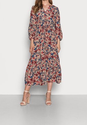 Geblümtes Kleid mit roten, blauen und beigen Mustern, einem V-Ausschnitt, langen Ärmeln und einem gestuften Rock. Kombiniert mit nudefarbenen Sandalen mit Blockabsatz.