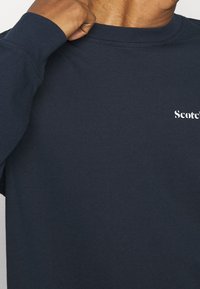 Navy blue long-sleeve t-shirt made of cotton. Features a crew neckline and a white text logo on the chest. Soft, textured fabric.