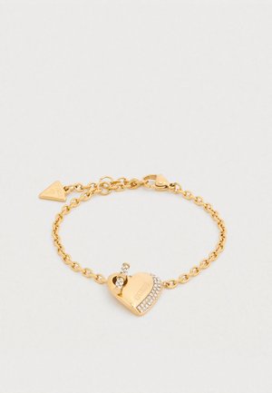 Βραχιόλι από χρυσό με γοητεία σε σχήμα καρδιάς με κούμπωμα και κρυσταλλικά διακοσμητικά. Οι κρίκοι είναι κυκλικοί, δημιουργώντας μια υφή εμφάνιση.