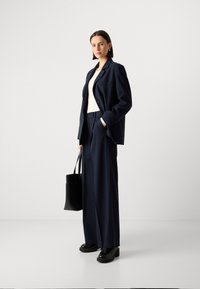 Blazer a righe navy e pantaloni a gamba larga, abbinati a una maglietta bianca. Borsa tote nera e scarpe con plateau completano il look professionale.