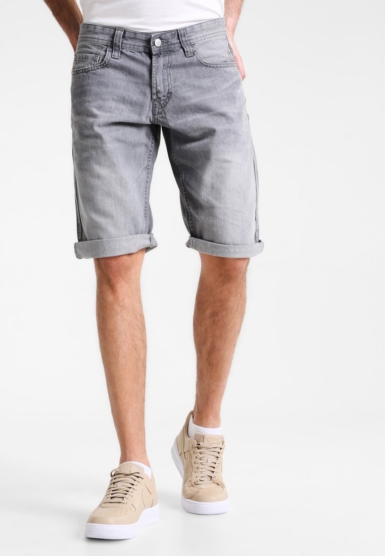 Shorts en denim gris avec des ourlets roulés, comportant cinq poches et un léger effet usé, portés avec des sneakers beiges. Texture lisse, design décontracté.