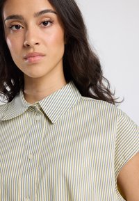 Short-sleeve collared blouse in light yellow with blue vertical stripes, featuring a button detail and a smooth, soft texture.
